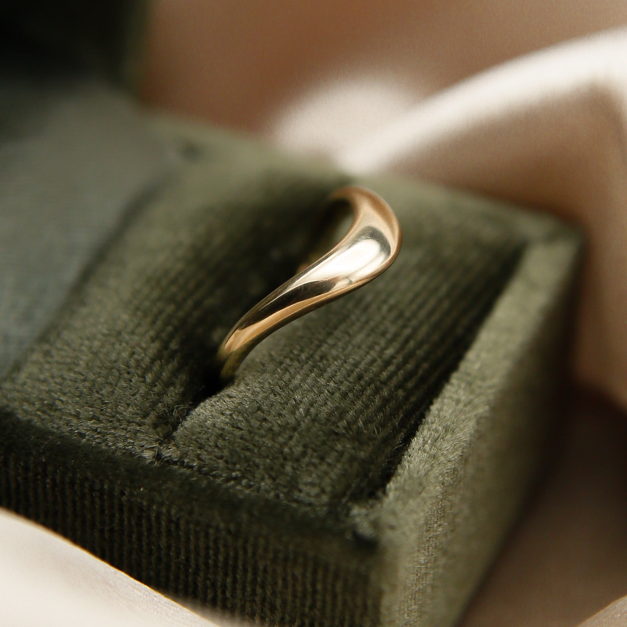 A wave style wedding band in gold, displayed on a green velvet box.