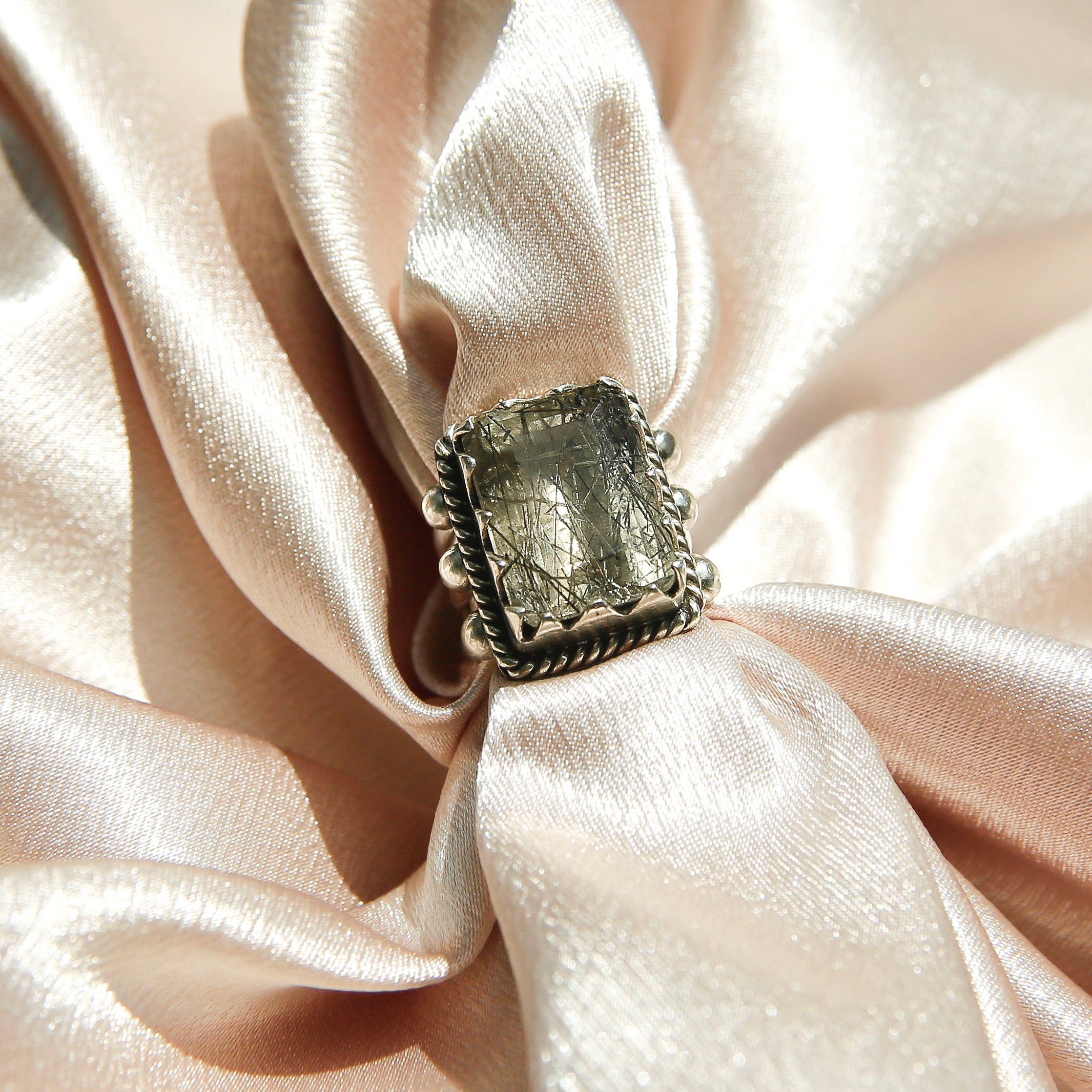 Sterling silver 3 band ring with a rectangular rutilated quartz stone. This ring has a bezel like setting made of sharp edges and a rope frame that has been patinated. Sold by Cival Collective in Milwaukee Wisconsin.