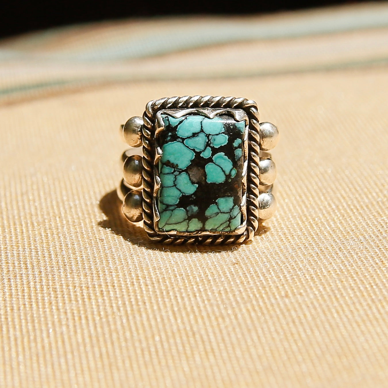 Sterling silver 3 band ring with a rectangular turquoise stone. This ring has a bezel like setting made of sharp edges and a rope frame that has been patinated. Sold by Cival Collective in Milwaukee Wisconsin.