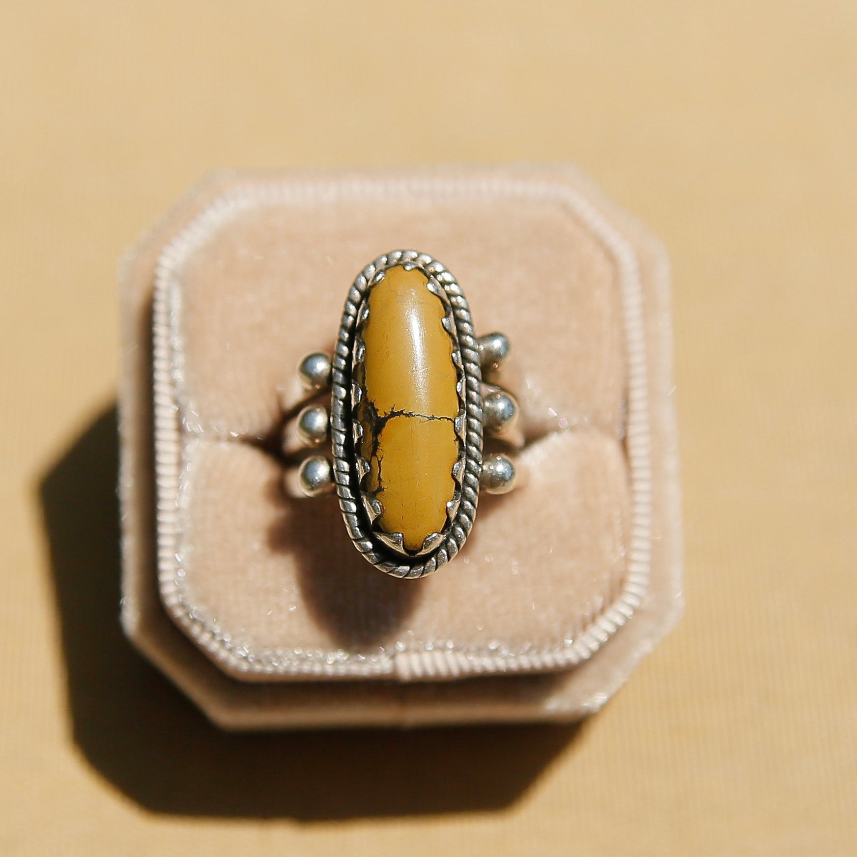 Sterling silver 3 band ring with a long oval yellow/tan stone. This ring has a bezel like setting made of sharp edges and a rope frame that has been patinated. Sold by Cival Collective in Milwaukee Wisconsin.