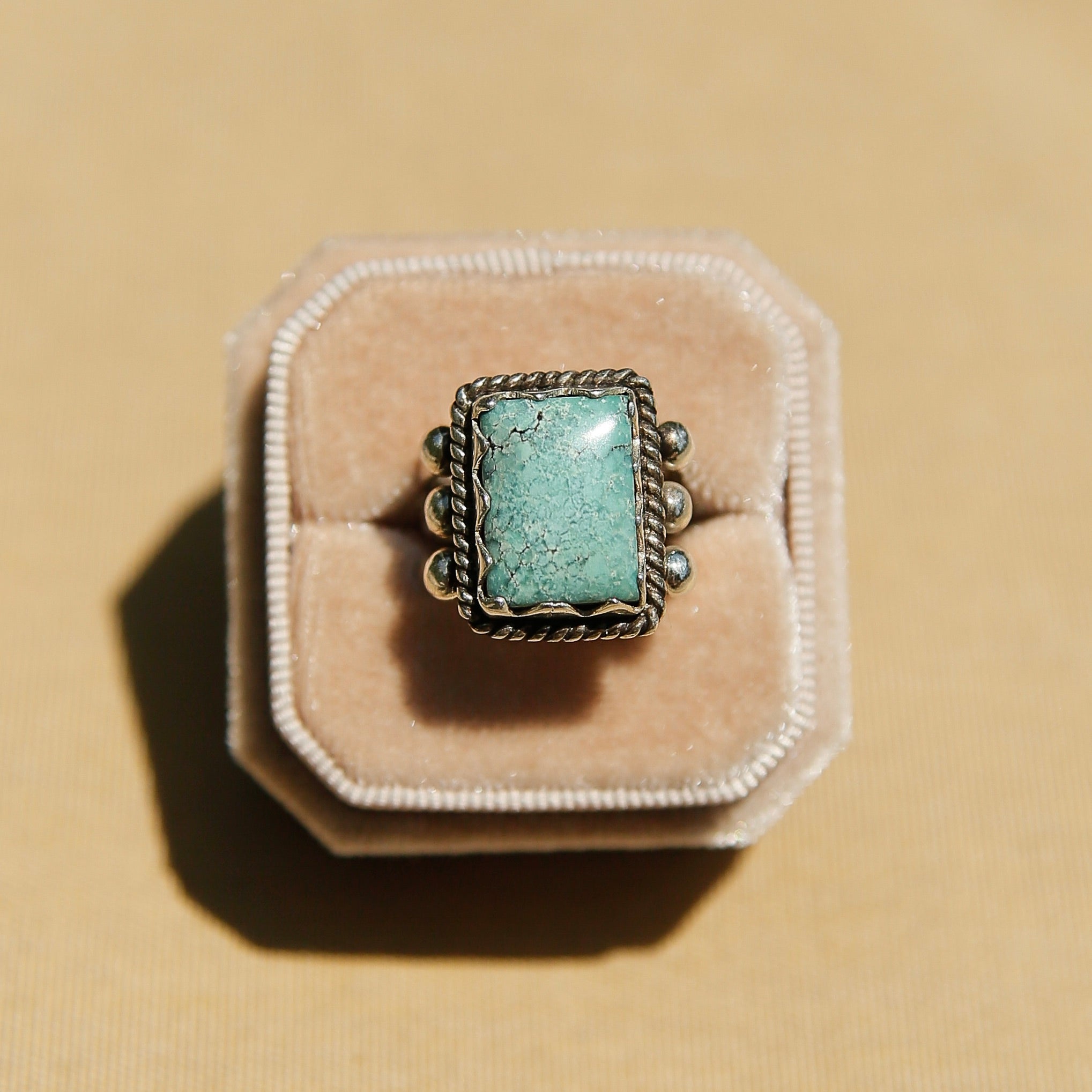 Sterling silver 3 band ring with a rectangular turquoise stone. This ring has a bezel like setting made of sharp edges and a rope frame that has been patinated. Sold by Cival Collective in Milwaukee Wisconsin.