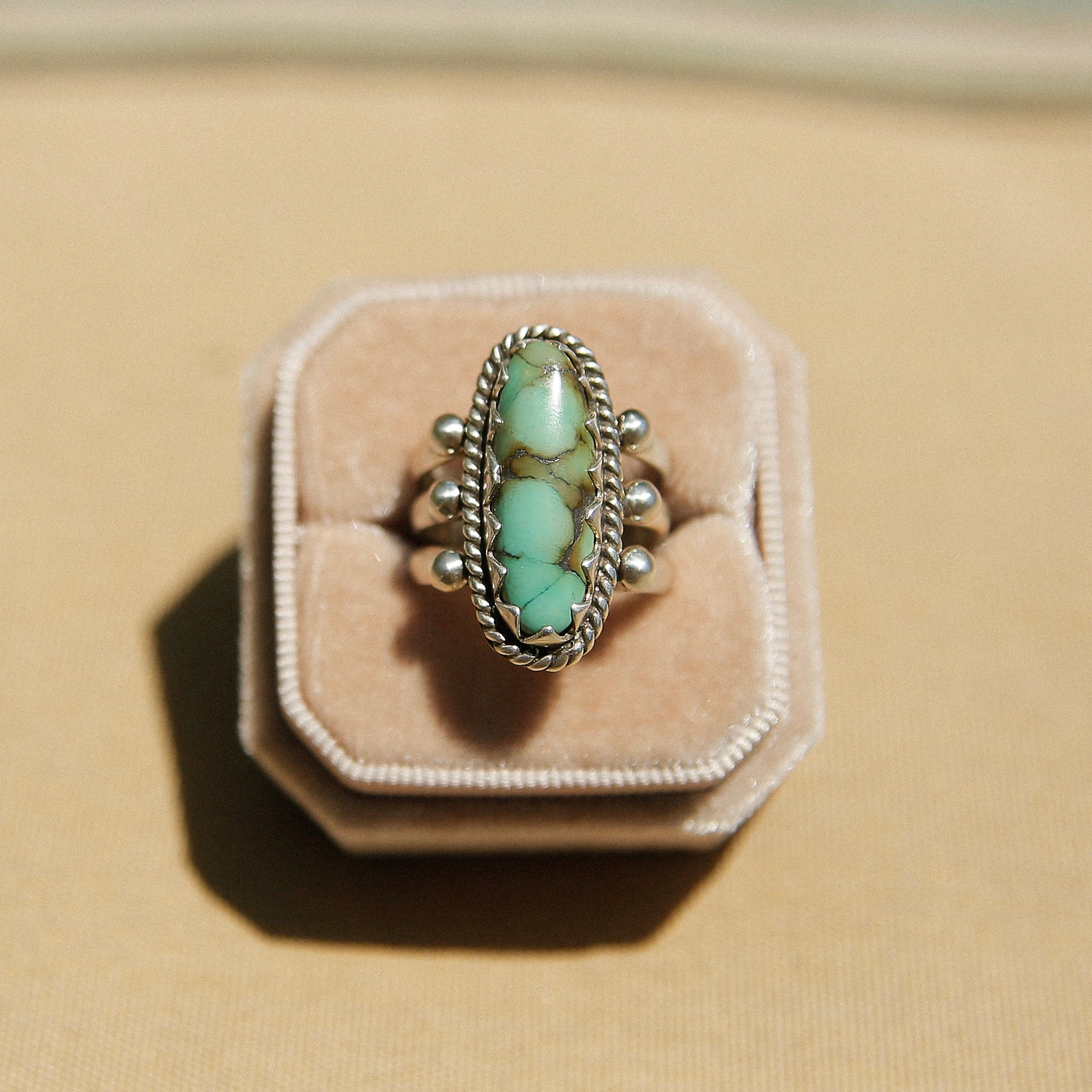 Sterling silver 3 band ring with a long oval turquoise stone. This ring has a bezel like setting made of sharp edges and a rope frame that has been patinated. Sold by Cival Collective in Milwaukee Wisconsin.