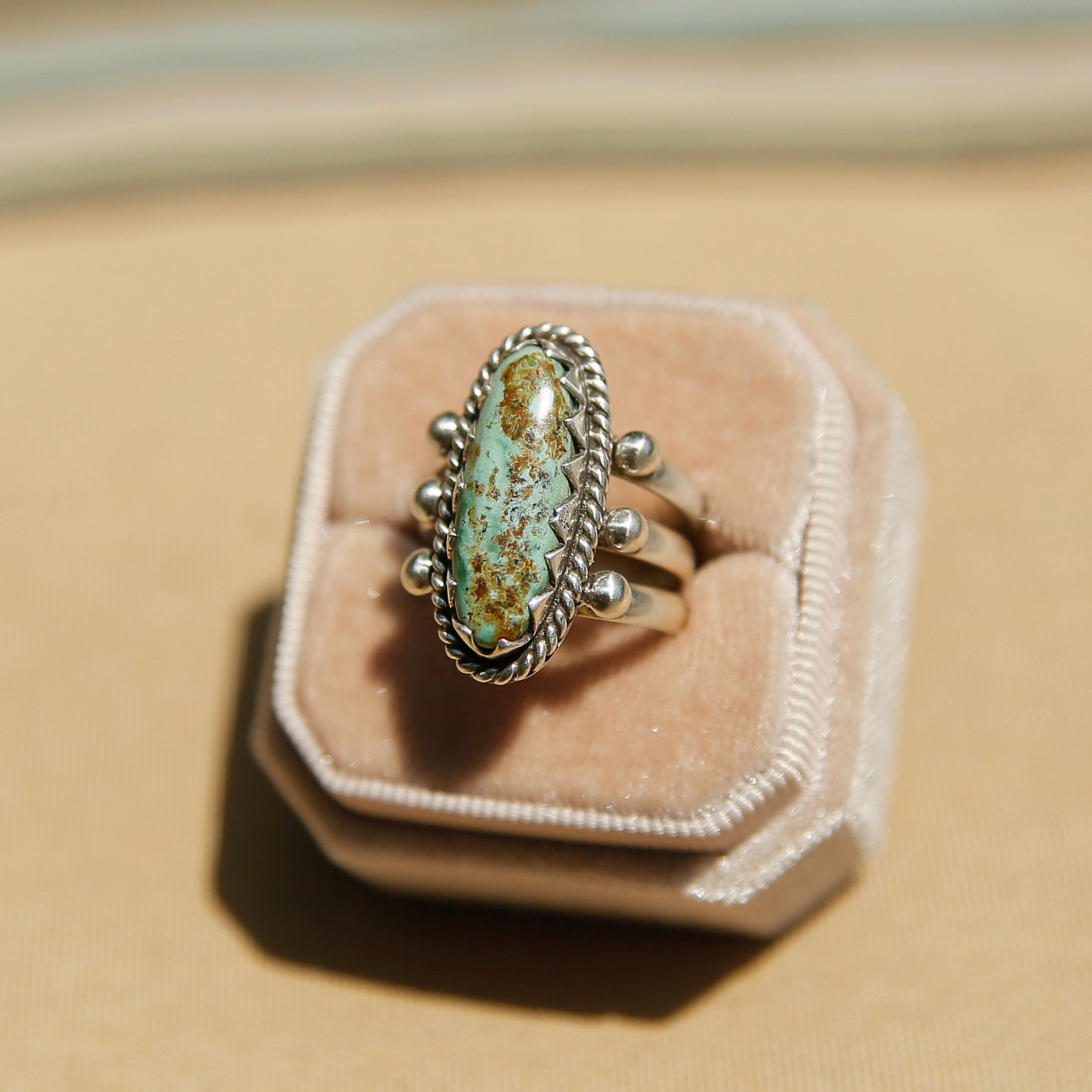 Sterling silver 3 band ring with a long oval turquoise stone. This ring has a bezel like setting made of sharp edges and a rope frame that has been patinated. Sold by Cival Collective in Milwaukee Wisconsin.