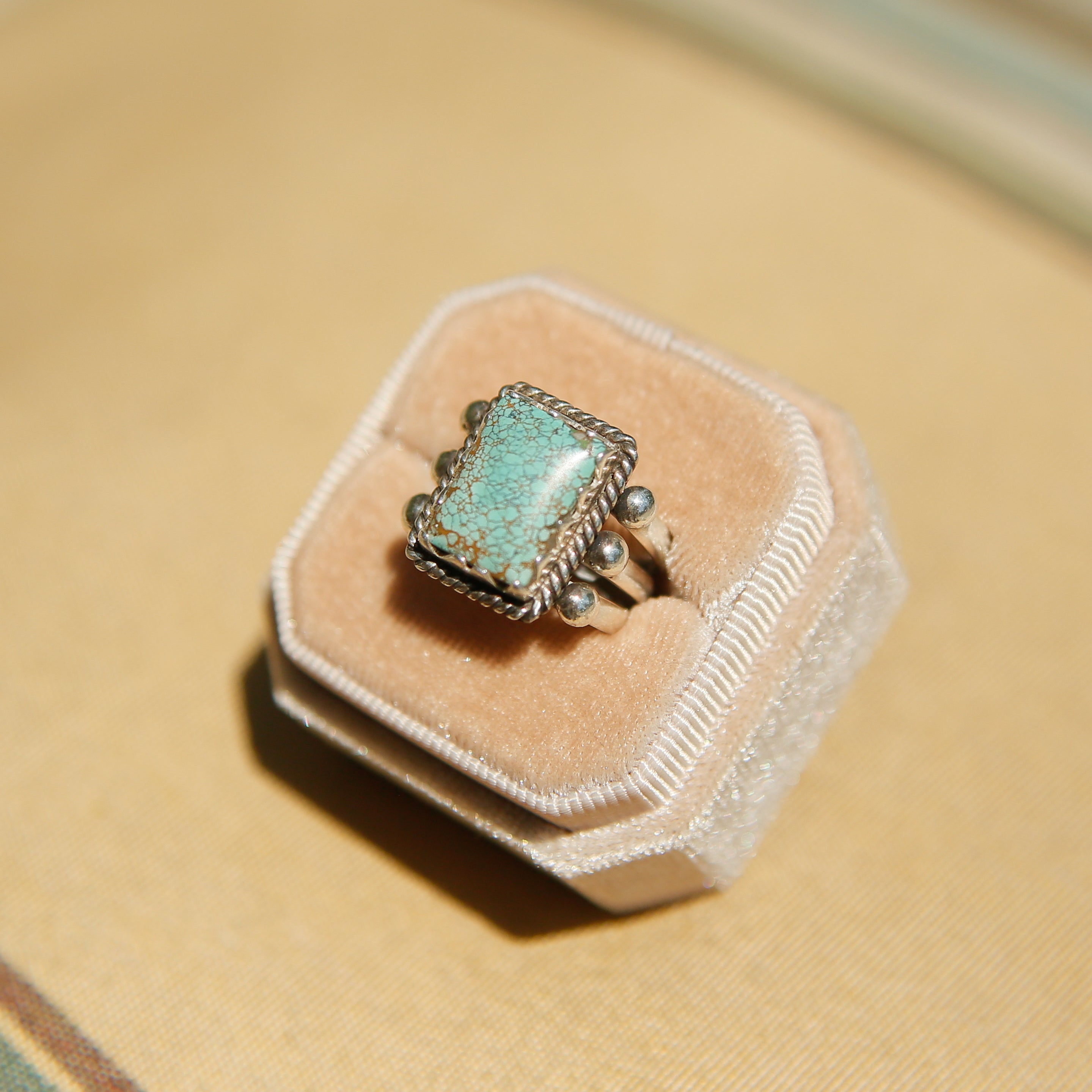Sterling silver 3 band ring with a rectangular turquoise stone. This ring has a bezel like setting made of sharp edges and a rope frame that has been patinated. Sold by Cival Collective in Milwaukee Wisconsin.