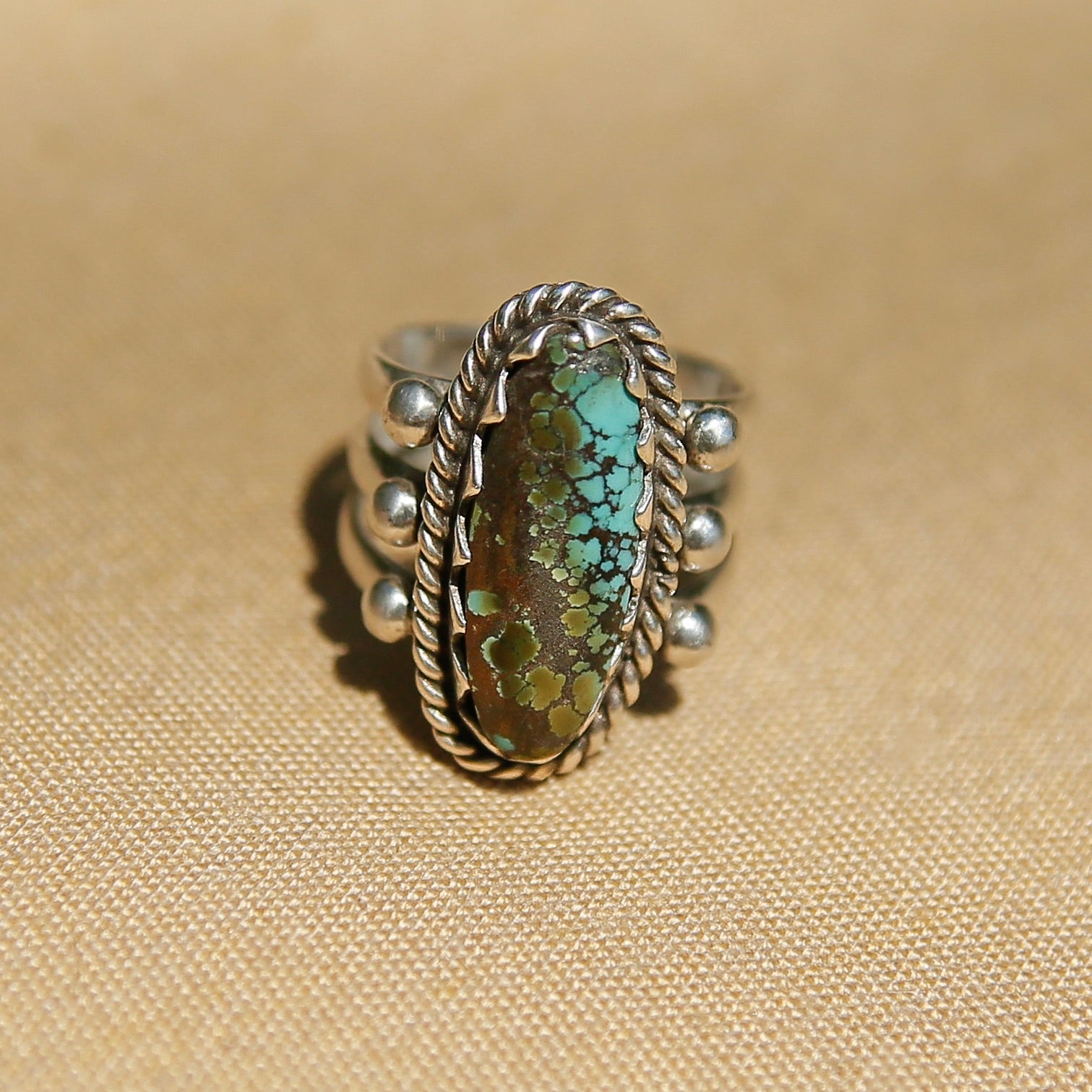 Sterling silver 3 band ring with a long oval turquoise stone. This ring has a bezel like setting made of sharp edges and a rope frame that has been patinated. Sold by Cival Collective in Milwaukee Wisconsin.