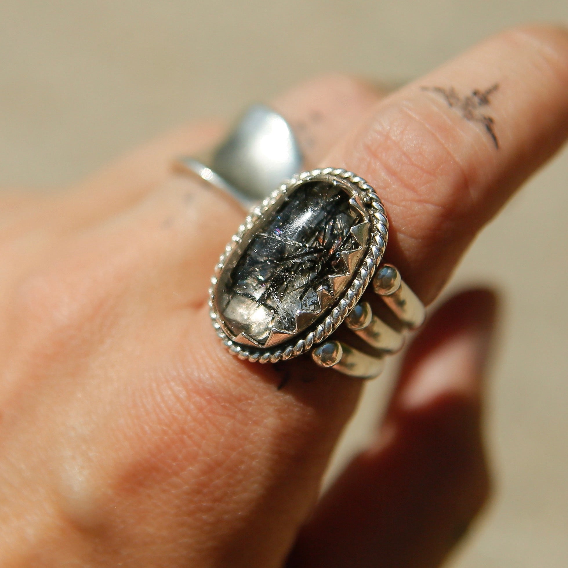 Sterling silver 3 band ring with an oval rutilated quartz stone. This ring has a bezel like setting made of sharp edges and a rope frame that has been patinated. Sold by Cival Collective in Milwaukee Wisconsin.