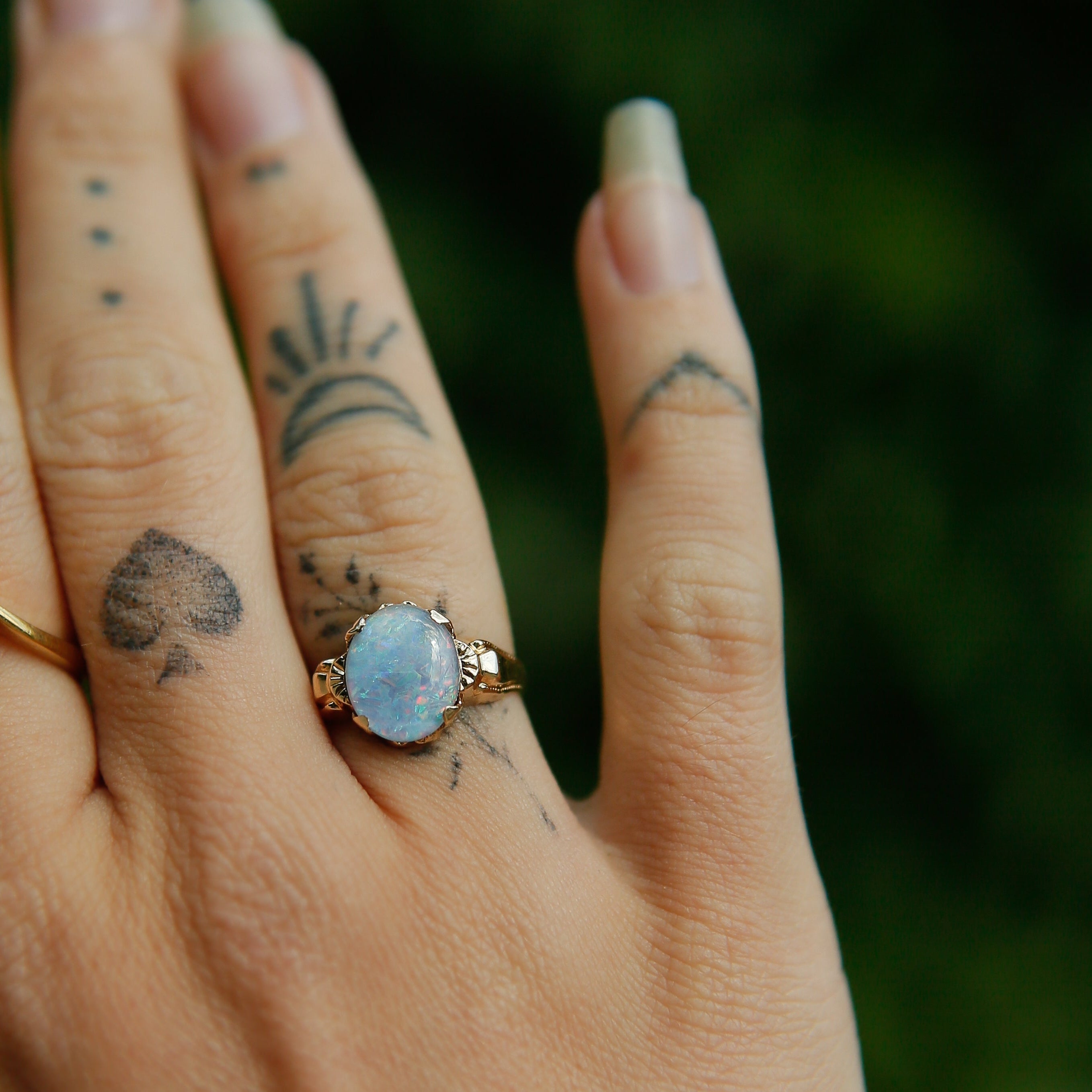 Hand with two rings, one gold and one blue, against a blurred green background