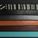 Six strips of leather displaying color options for the "Ace" leather bracelet, the colors are Black & white fabric, Black leather, gunmetal gray leather, tan leather, mahogany leather and turquoise leather.