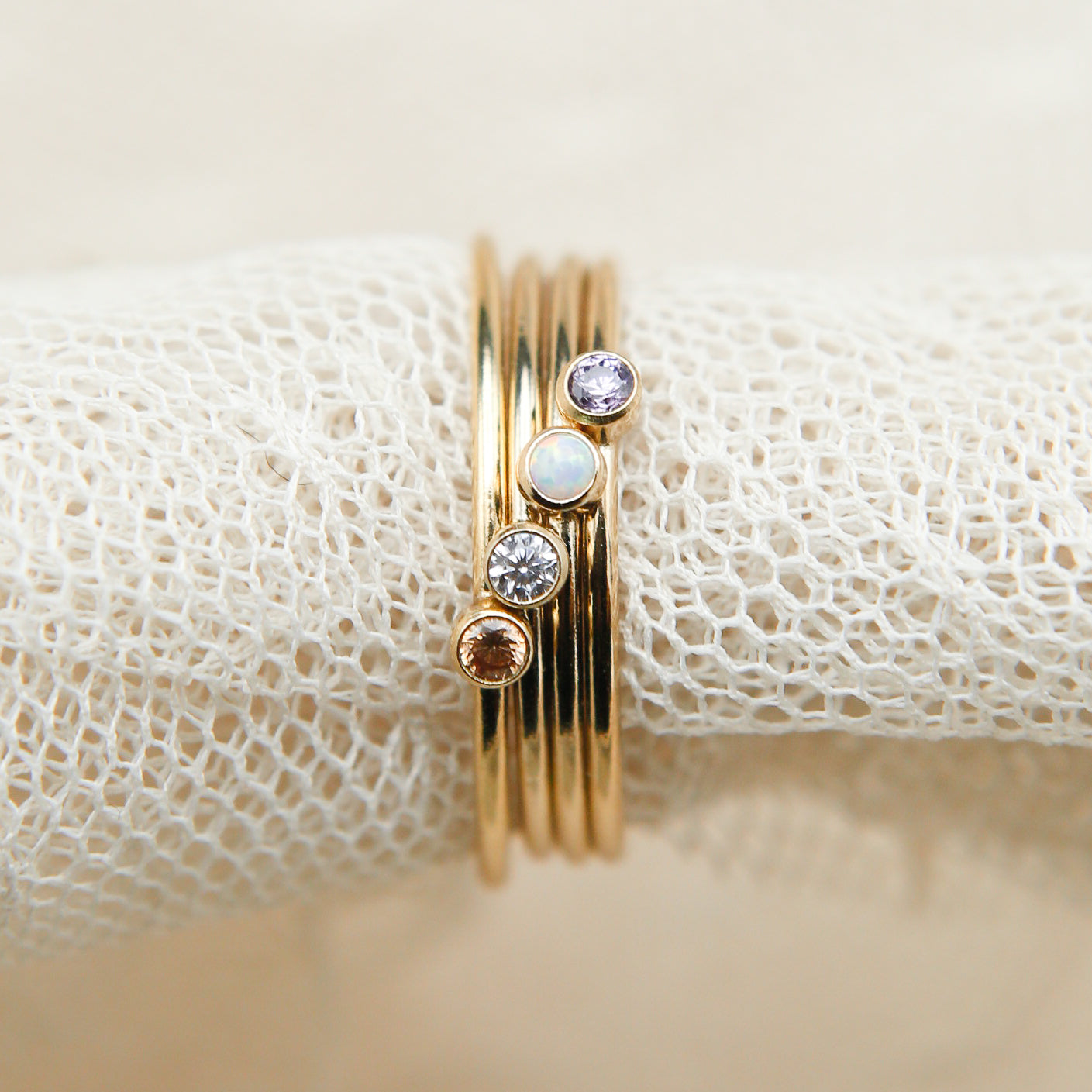 Four gold stacking rings stacked together with four different stones , left to right is brown, grey, opal, purple