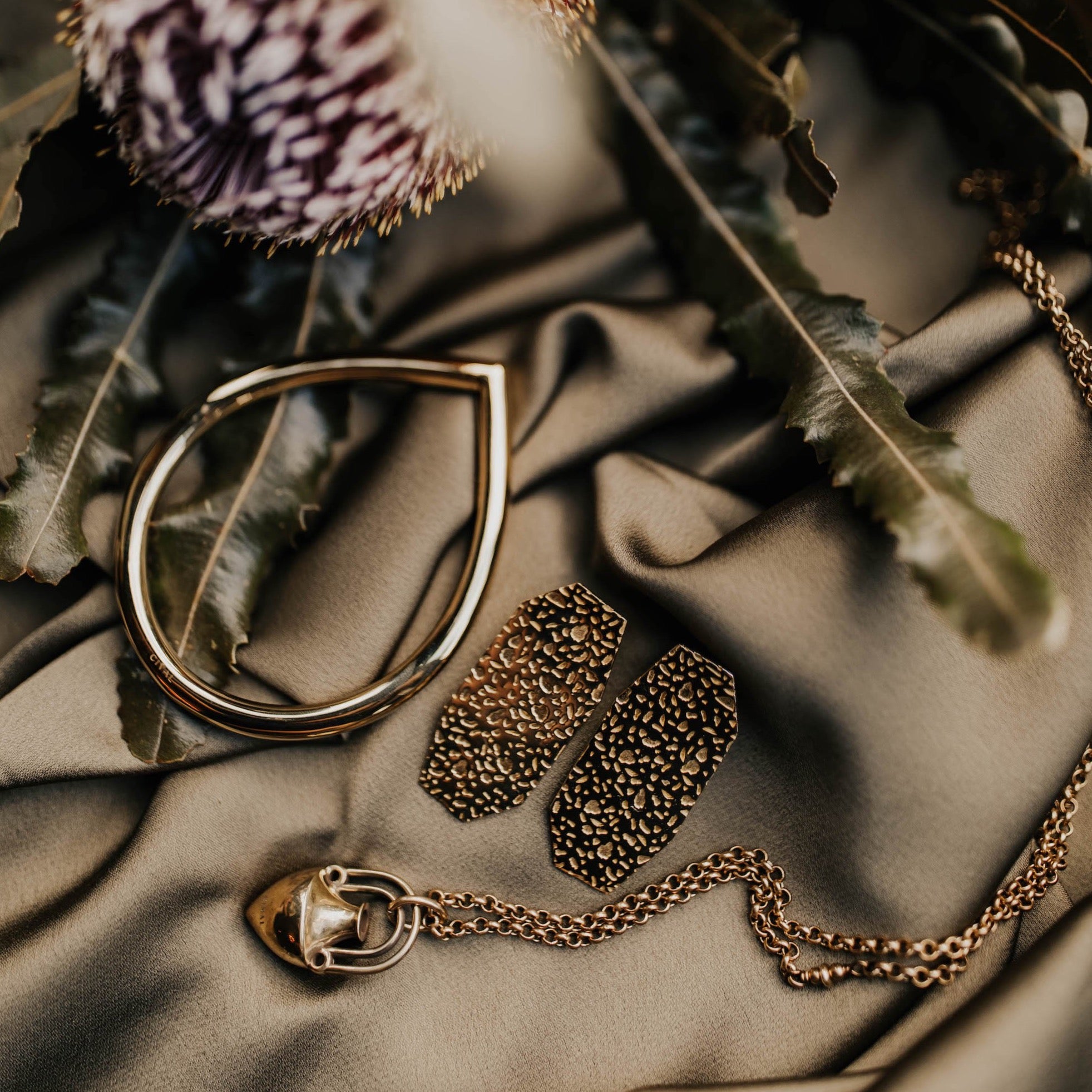 brass bangle laid on a cloth aesthetically next to a brass necklace and brass earrings