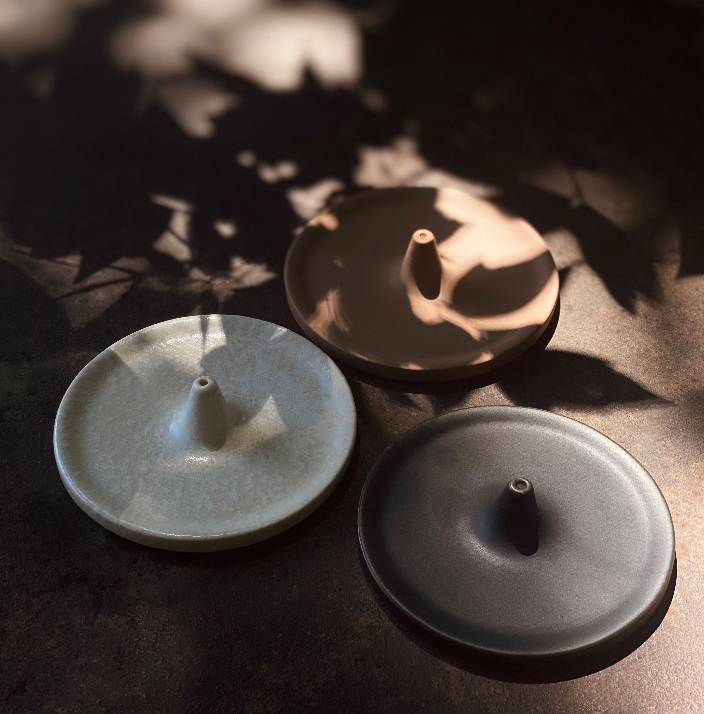 Image of three round 4" incense burners, variety of black, light pink, and white.
