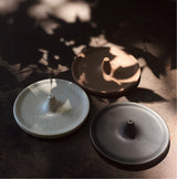 Image of three  round 4" incense burners, variety of black, light pink, and white. 