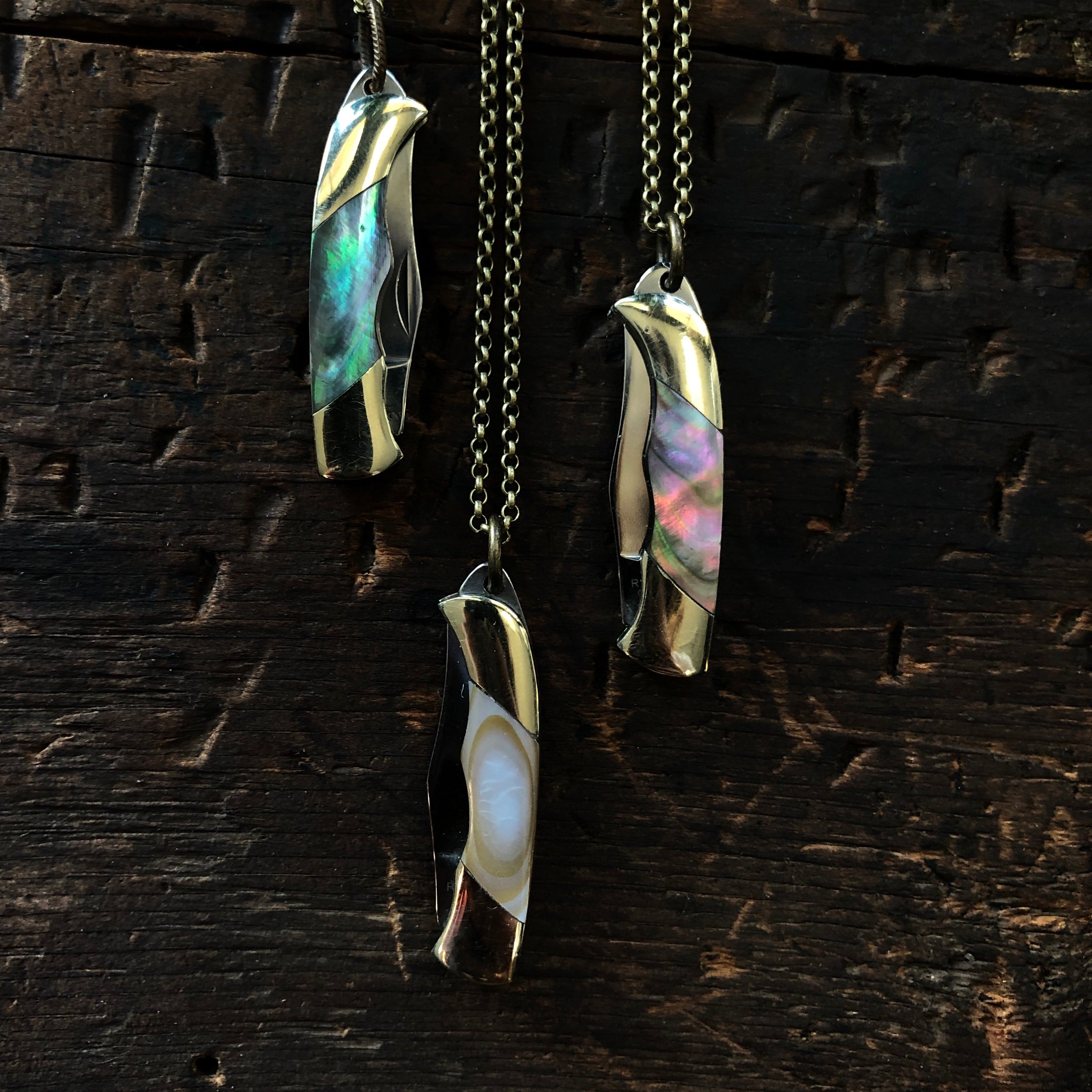 Three brass pocket knife necklaces, blades tucked in. Hanging on brass chain