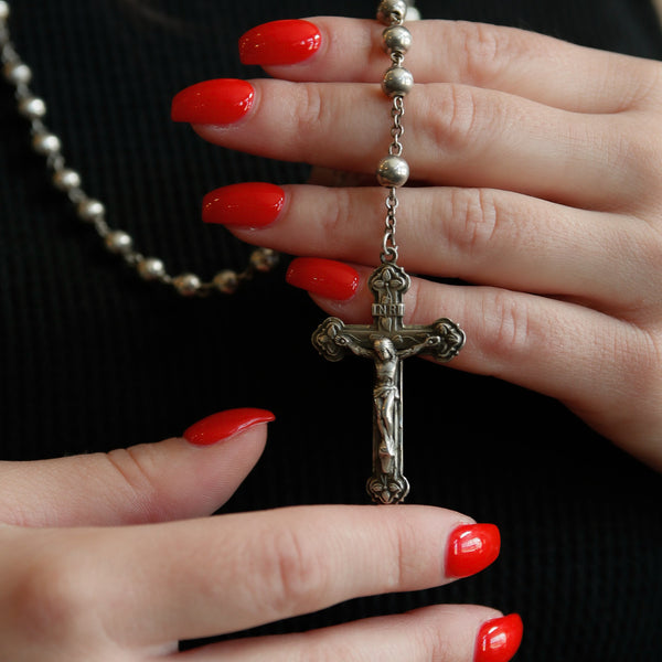 close up of a model's hands holding an antique sterling silver cross necklace with rosary beads 