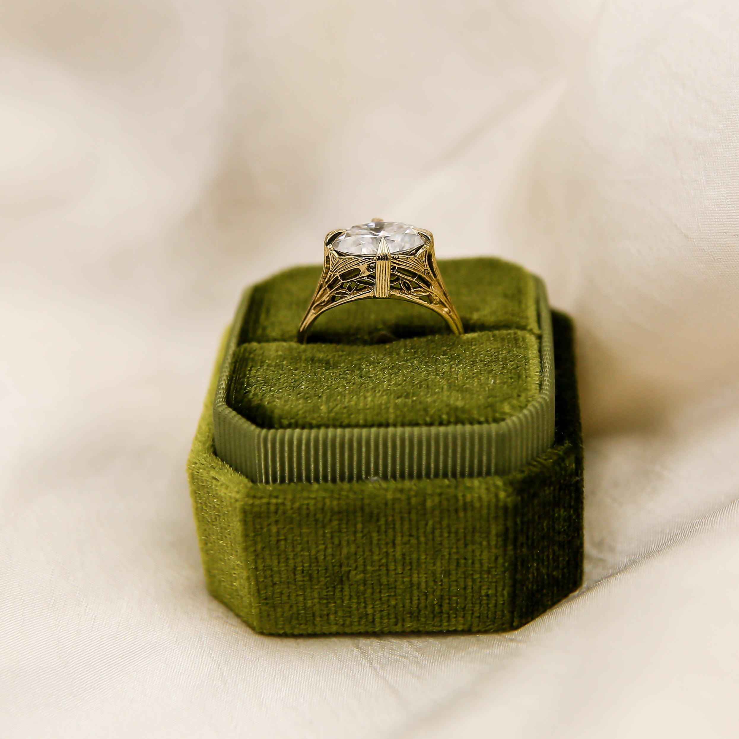 Gold ring with a diamond on a green velvet cushion against a white background