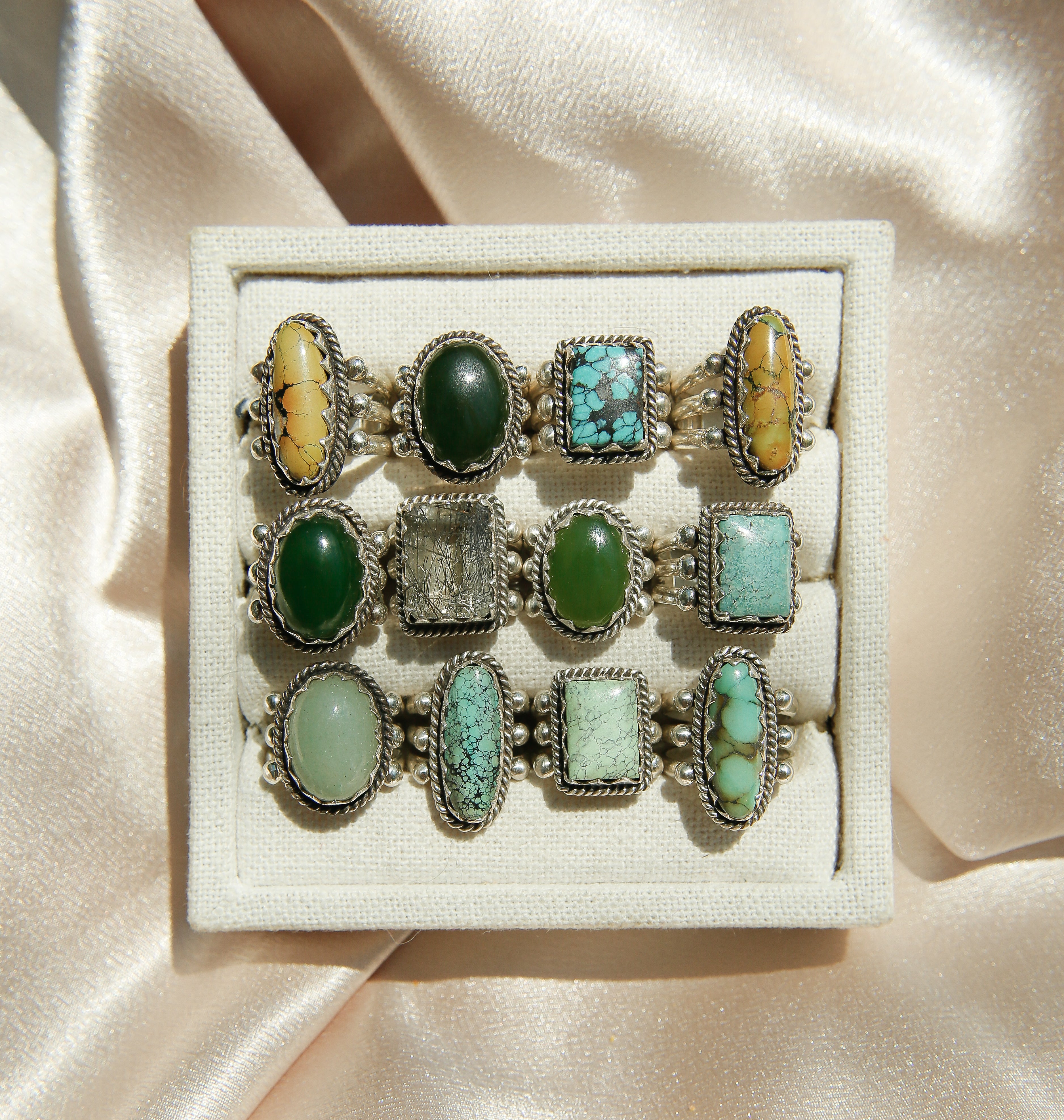 Set of rings with green, turquoise and yellow-green stones on a beige fabric background