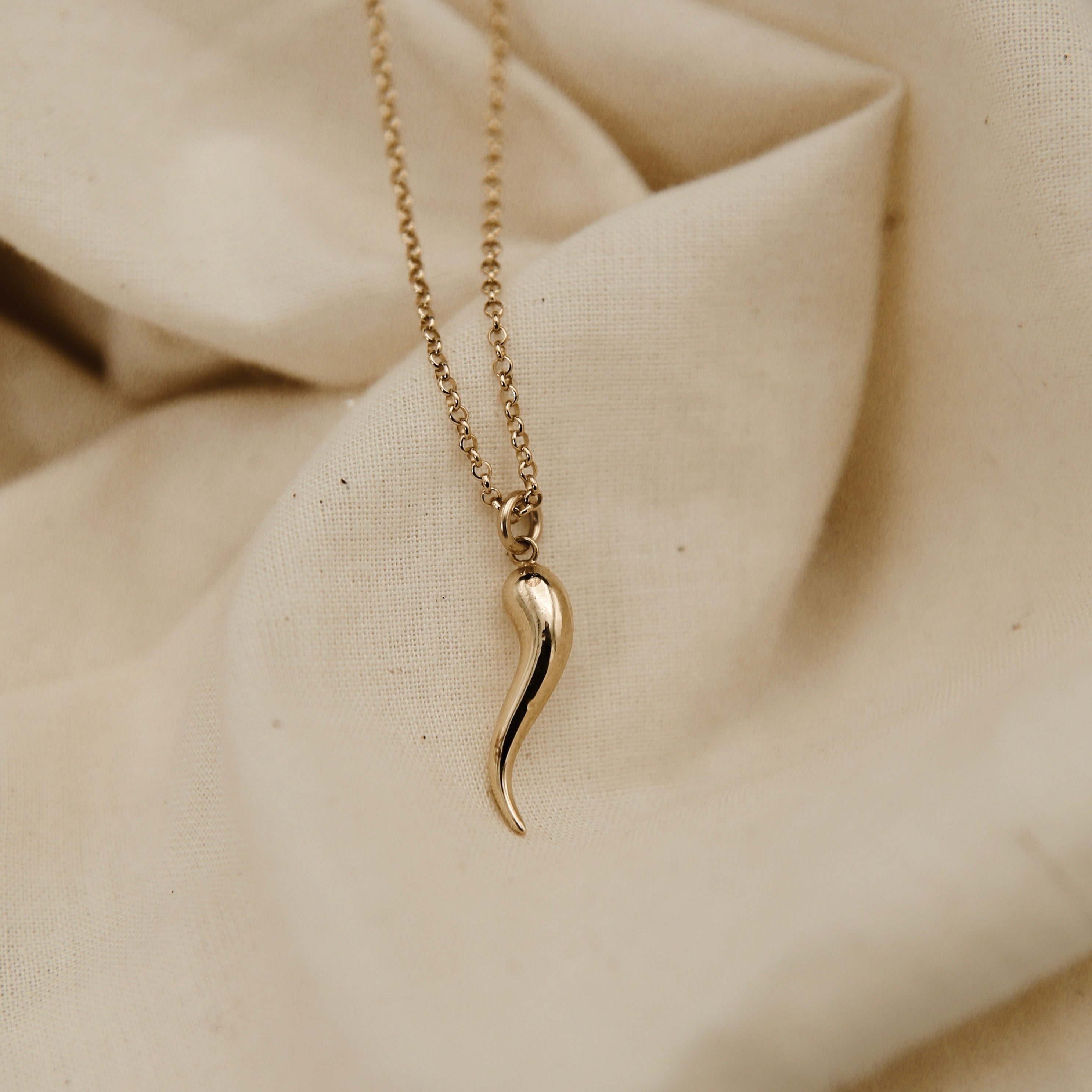 Gold necklace with a unique pendant on a beige fabric background