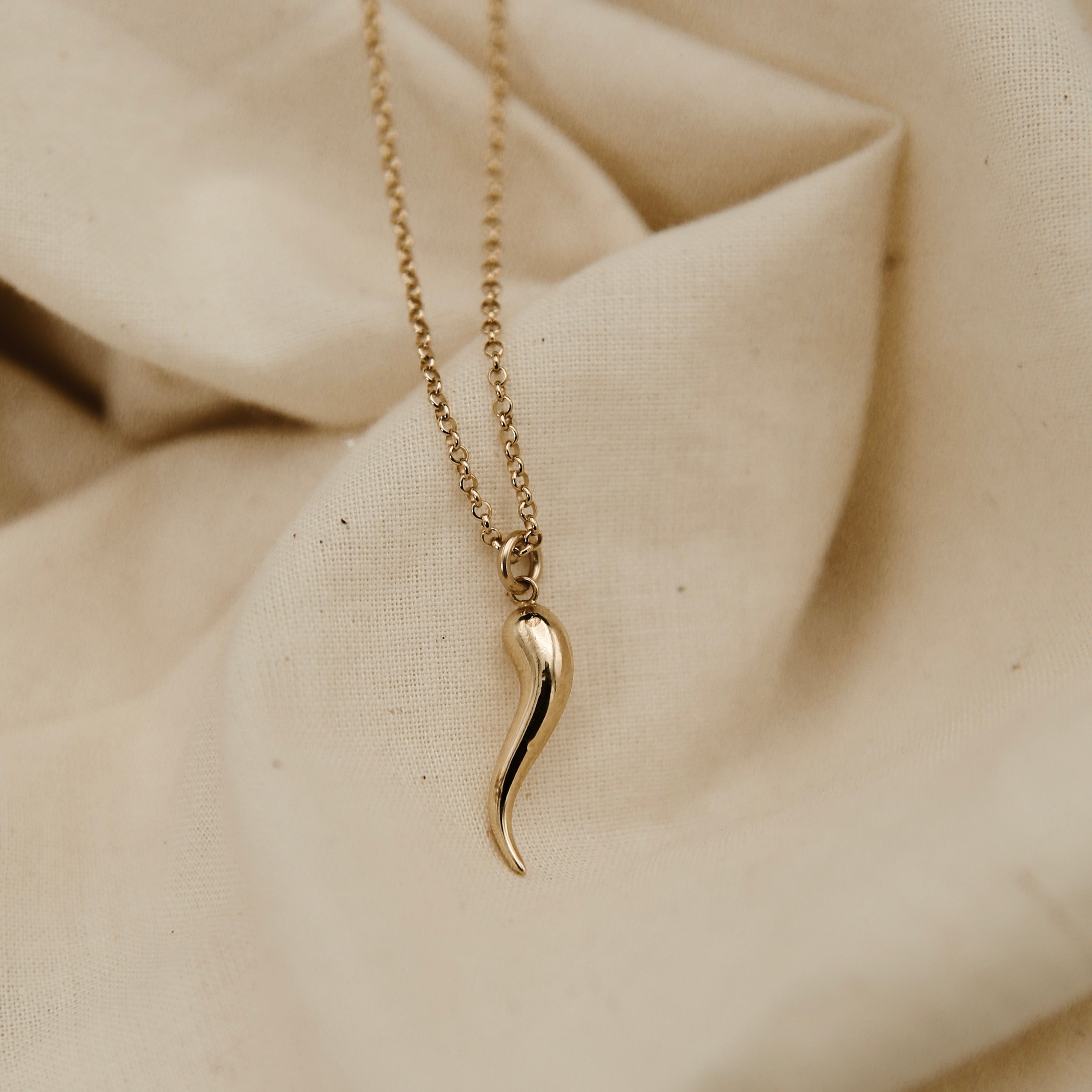 Gold necklace with a unique pendant on a beige fabric background