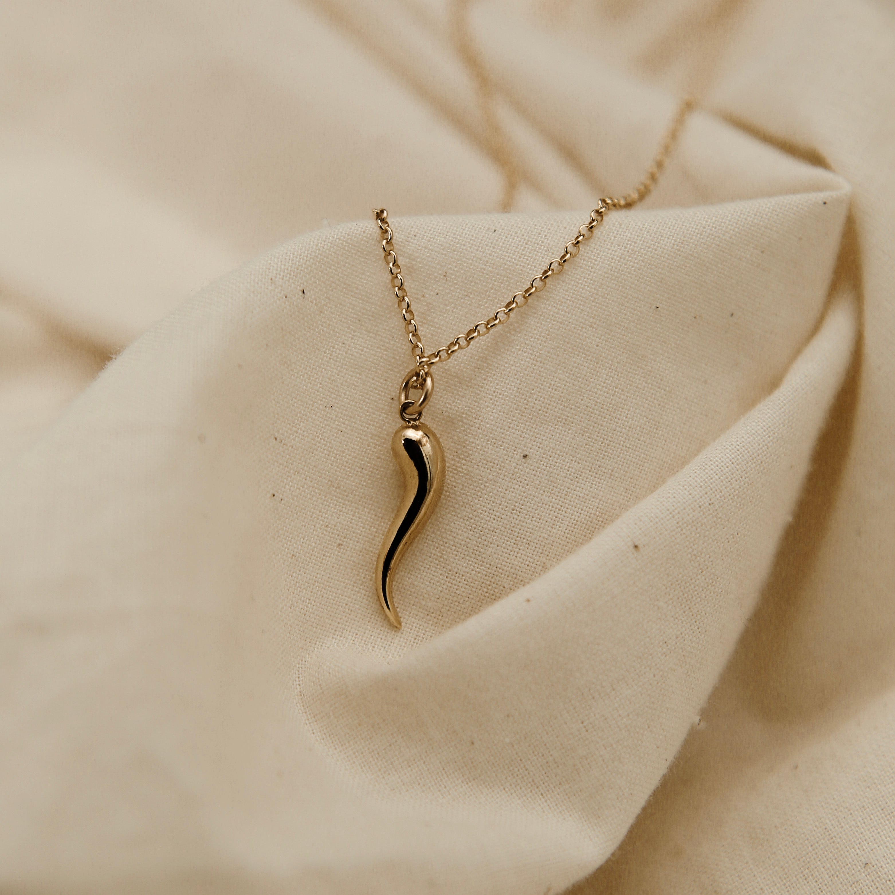Gold necklace with a unique pendant on a beige fabric background