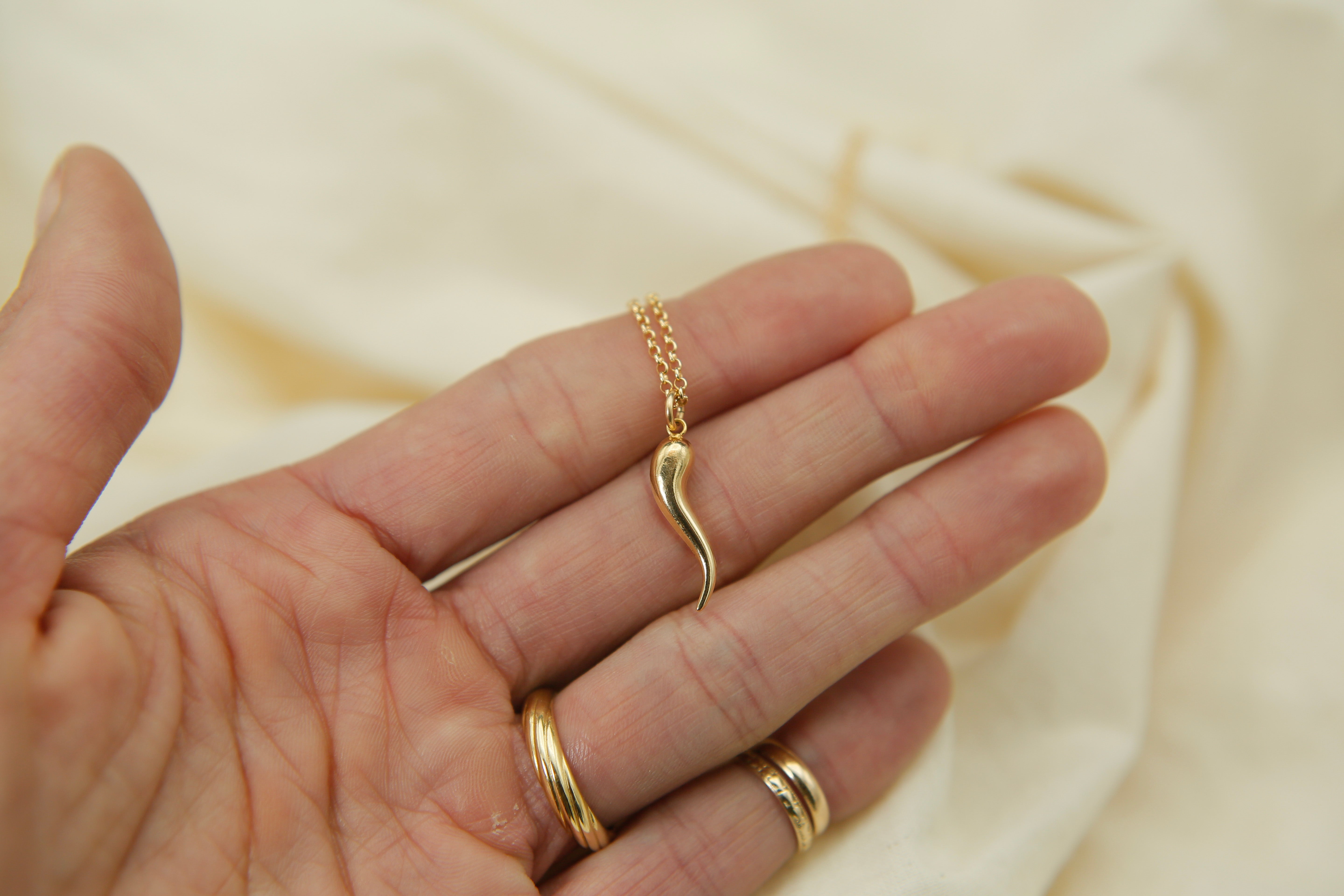 Gold necklace and rings on a hand with a beige fabric background