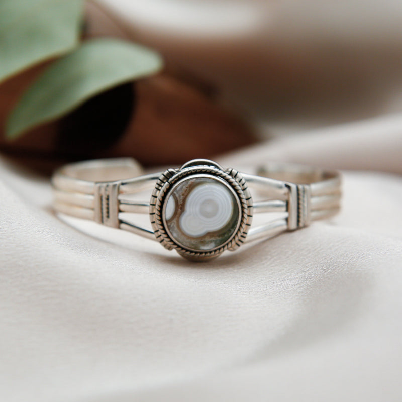 Close up of a sterling silver cuff featuring an oval Ocean Jasper center stone. The stone is bezel set with twisted & stamped silver details.