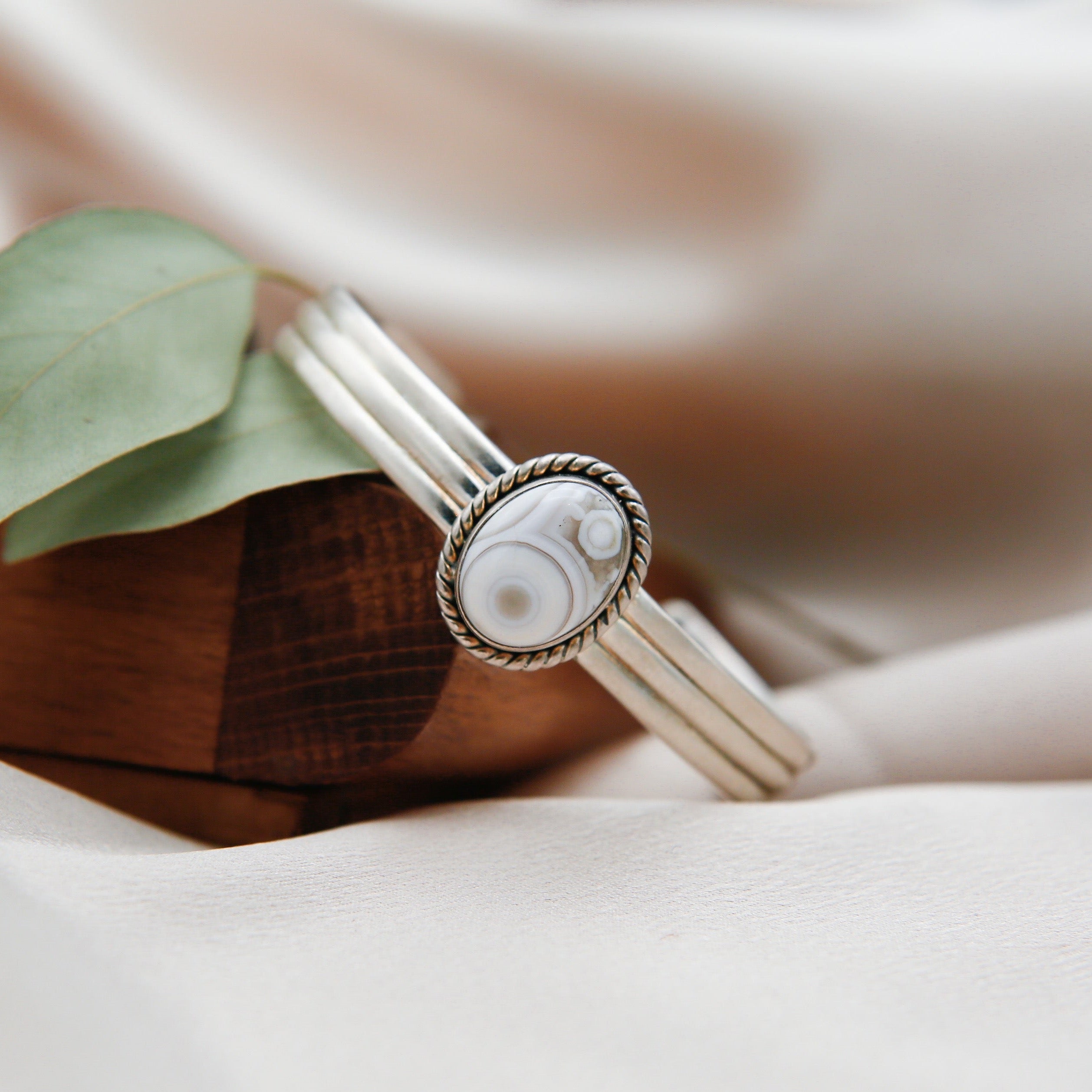 a sterling silver cuff featuring a white ocean jasper center stone. the cuff features a twisted bezel and stamped silver details