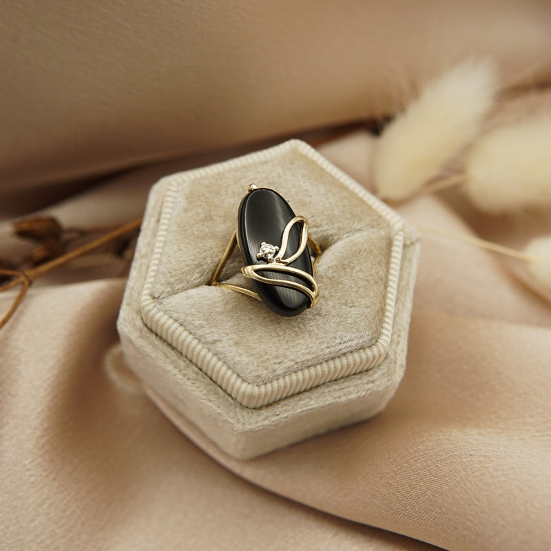 A unique vintage black onyx ring with a decorative leaf edge design. The center is set with a petite melee single cut diamond accent— bead set in a mill grain trim- centered in onyx oval, on a 10K yellow gold band. 