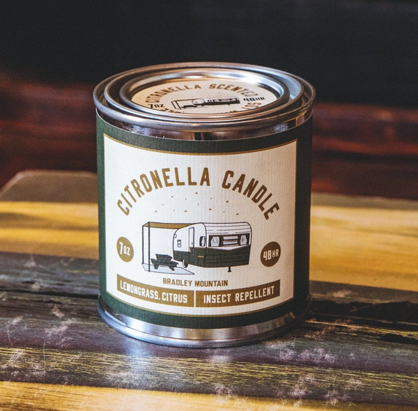 Image of candle tin on dark wooden countertop. Tin has image of vintage camper on the from and reads "citronella candle, lemongrass.citrus, insect repellent" 48 hour