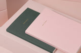 A light pink and a green "note to self" journal displayed stacked on top of each other.