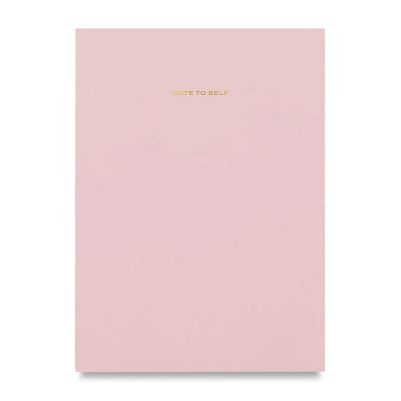 Light pink "Note to Self" journal made by Wit & Delight. Pink notebook on white background, words "note to self" printed in gold at top center of cover. 