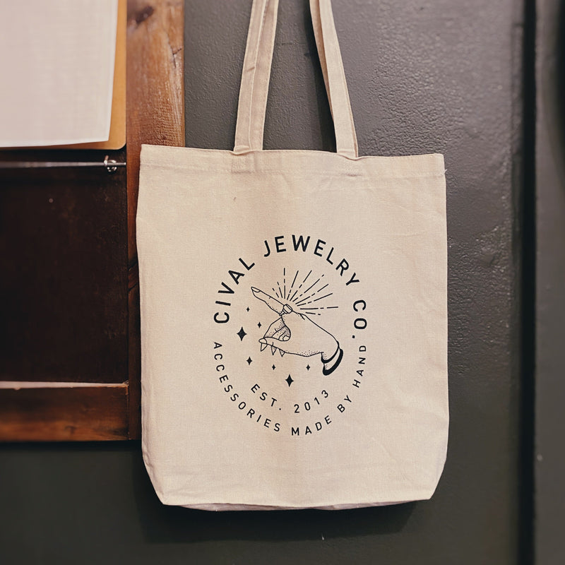 image of natrual cotton canvas tote with cival jewelry co screen printed on from. Image of hand with large ring with starburst emitting from ring and star embellishments.Heavy natural cotton canvas  14x16x3" bag with 8" handles  