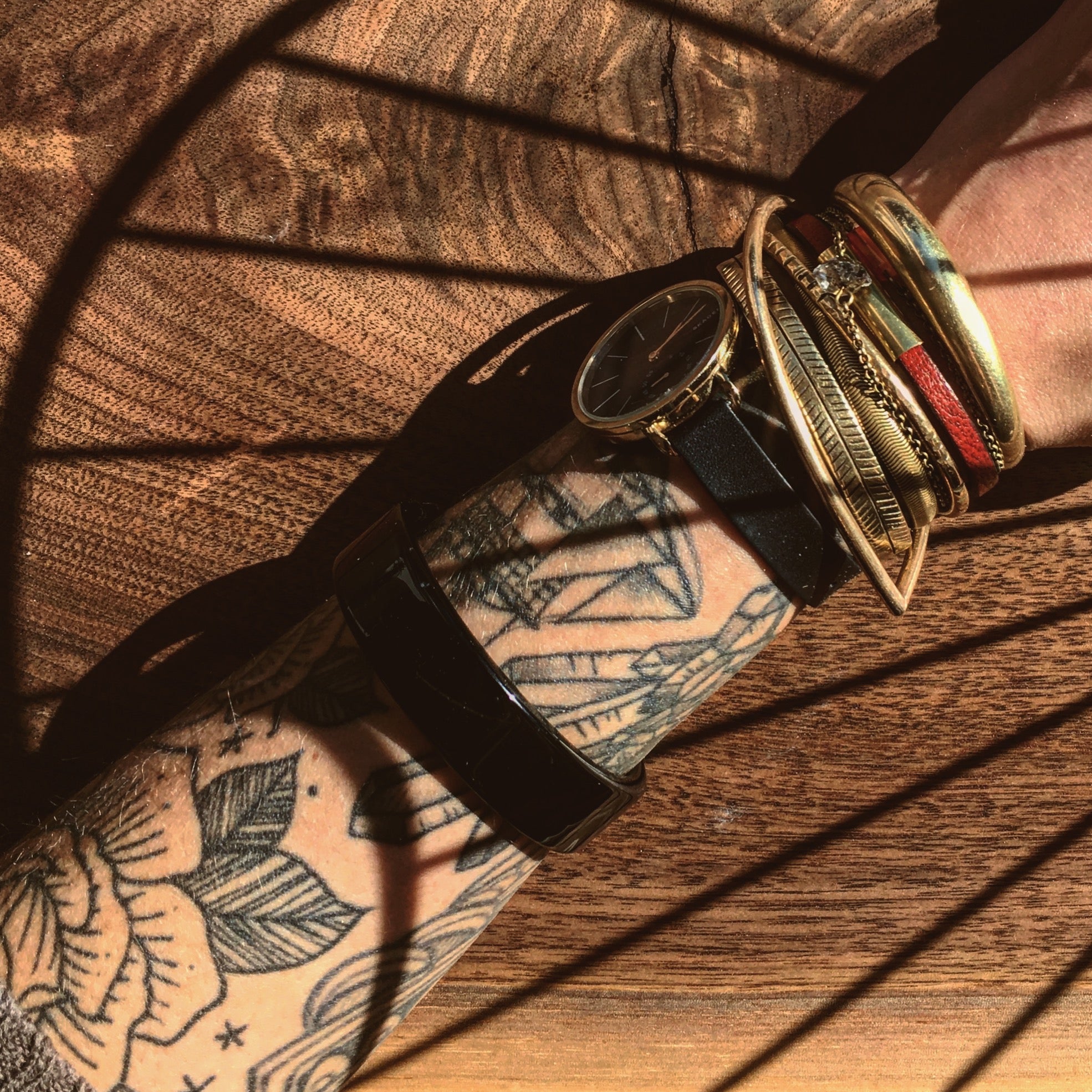 Model's wrist wearing a watch and a collection of CIVAL Collective brass layering bracelets including a blood orange leather & brass bar "Aida" bracelet.