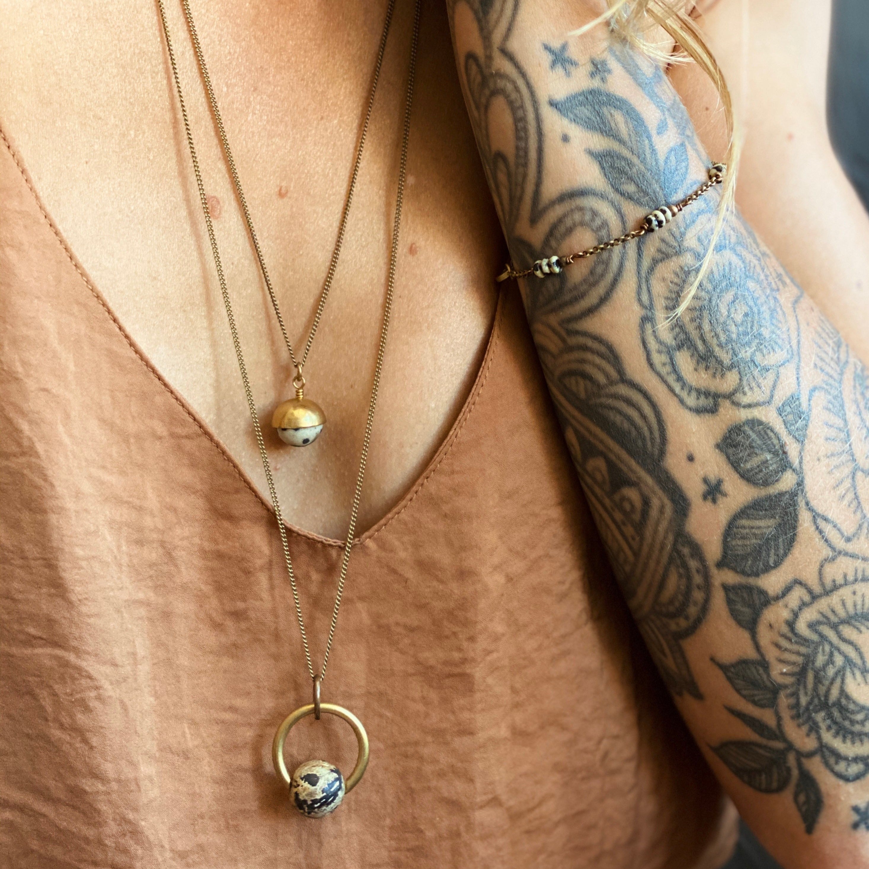 Model wearing Dalmatian jasper beaded bracelet, long suspension necklace with jasper stone, and a 22 inch "Coco" necklace that has a small Dalmatian jasper round stone capped in brass. 