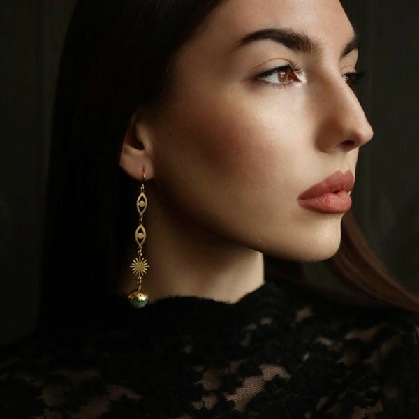 photo of eria earrings on model, brass starburst and eye shaped hoop drops 