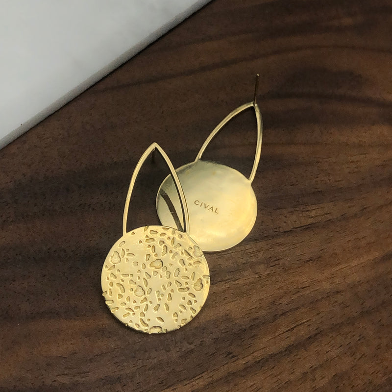 Close up of front and back of CIVAL's "Gwen" brass cast teardrop stud earrings that have a textured brass circle at the bottom of the open teardrop shape.