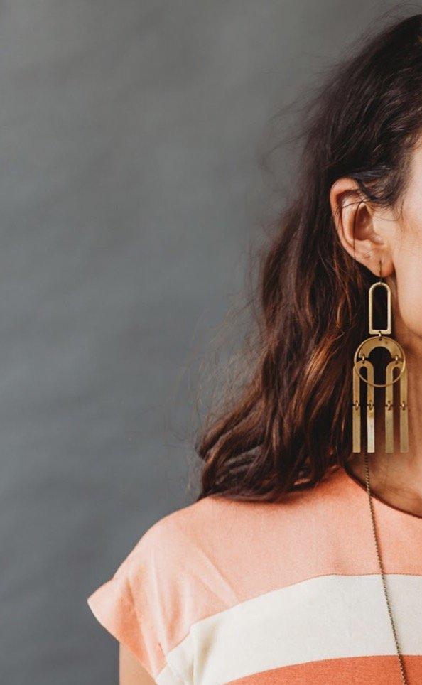 Model wearing CIVAL Collective's bright brass statement earrings comprised of modern brass shapes stacked and connected with jump rings creating a chandelier effect.