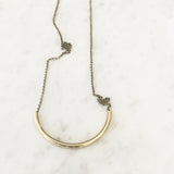 Close up of "Lydia" bright brass half circle tube necklace on rolo chain displayed flat on marble.