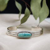 a sterling silver cuff with a east west facing royston turquoise center stone on a white cloth