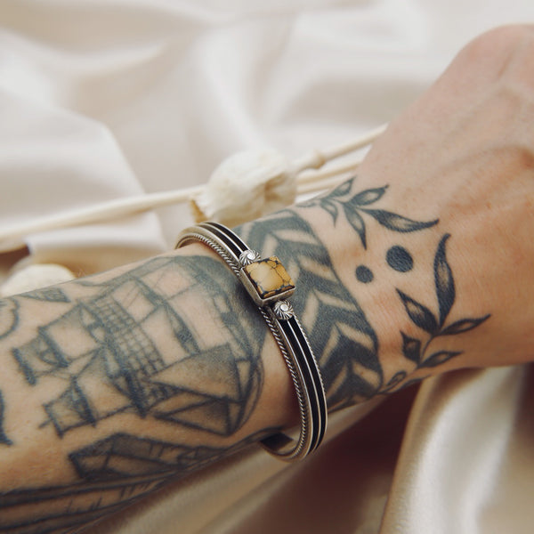 a sterling silver cuff featuring a yellow turquoise center stone on a model's wrist