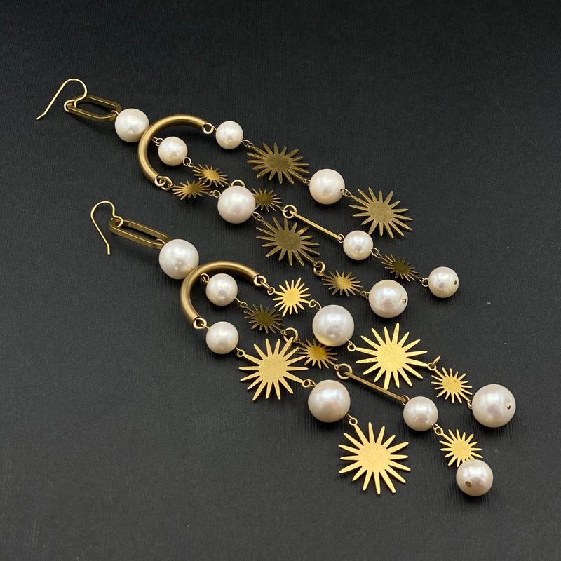 Cival Collective's large statement earrings made up of brass starburst components mixed with round natural pearl beads hanging in 3 different sections on each earring.