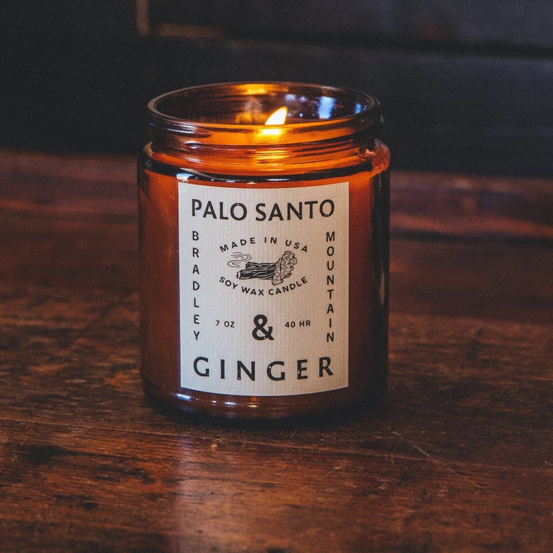 lit candle in amber colored jar, labeled "palo santo and ginger" 