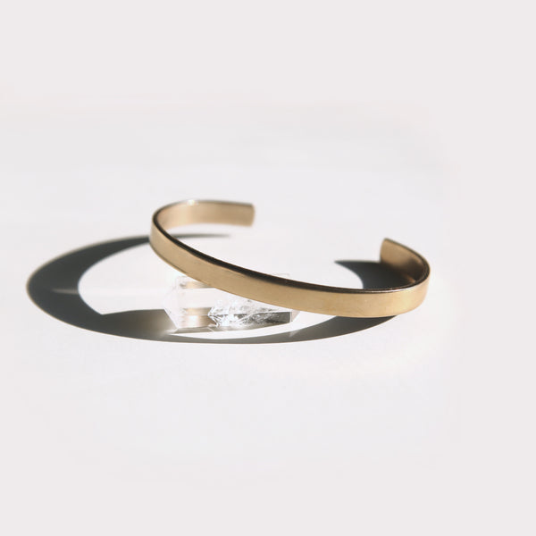 a solid brass cuff with a sleek and minimalistic design resting on a quartz stone