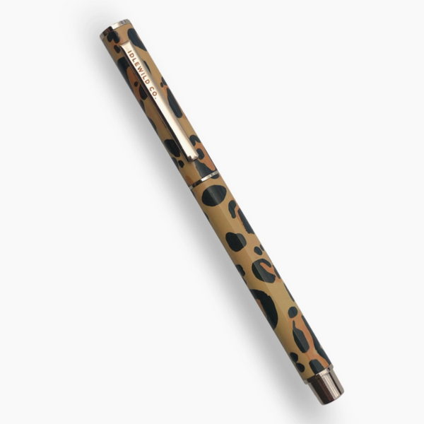 Image of pen on white background. pen has cheetah print on exterior and "idlewild co" printed on pen cap.  BLACK INK  • .5MM LINE WEIGHT  • APPROXIMATELY 5 1/4″ X 3/8″