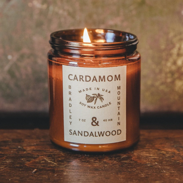 image of lit candle on top of dark wood countertop. Candle scented cardamom and sandalwood
