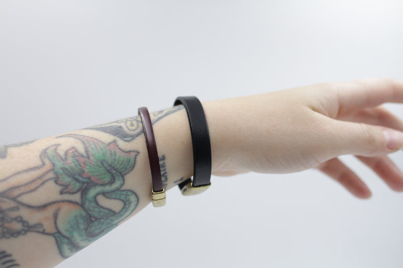 Model's wrist layered with the "Amie" mahogany leather bracelet and the "Ace" wide black leather bracelet, both designed by CIVAL Collective.