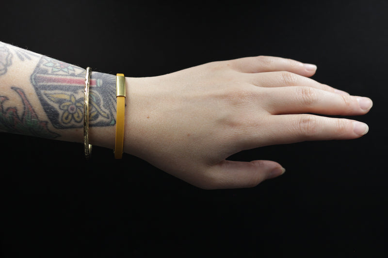 Model's wrist wearing CIVAL Collective's marigold leather "Aida" bracelet with 1" brass slider and layered with a textured brass bangle.