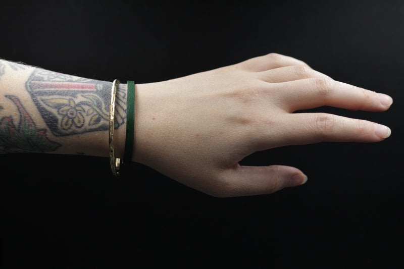 CIVAL Collective's "Aime" bracelet in bottle green leather displayed on model's wrist and layered with textured brass bangle.