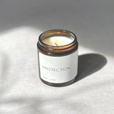 litle candle in amber glass jar, white label reading "protection magic candle" 