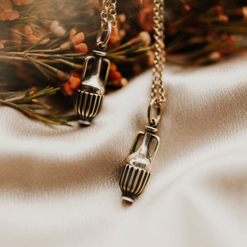 two necklaces that feature a solid cast brass vessel pendant on a brass chain