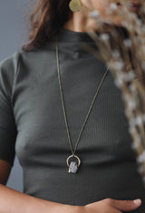 Model wearing long "Billie Rae" necklace that has a faceted tourmalinated quartz stone & small brass triangle suspended in open brass ring.